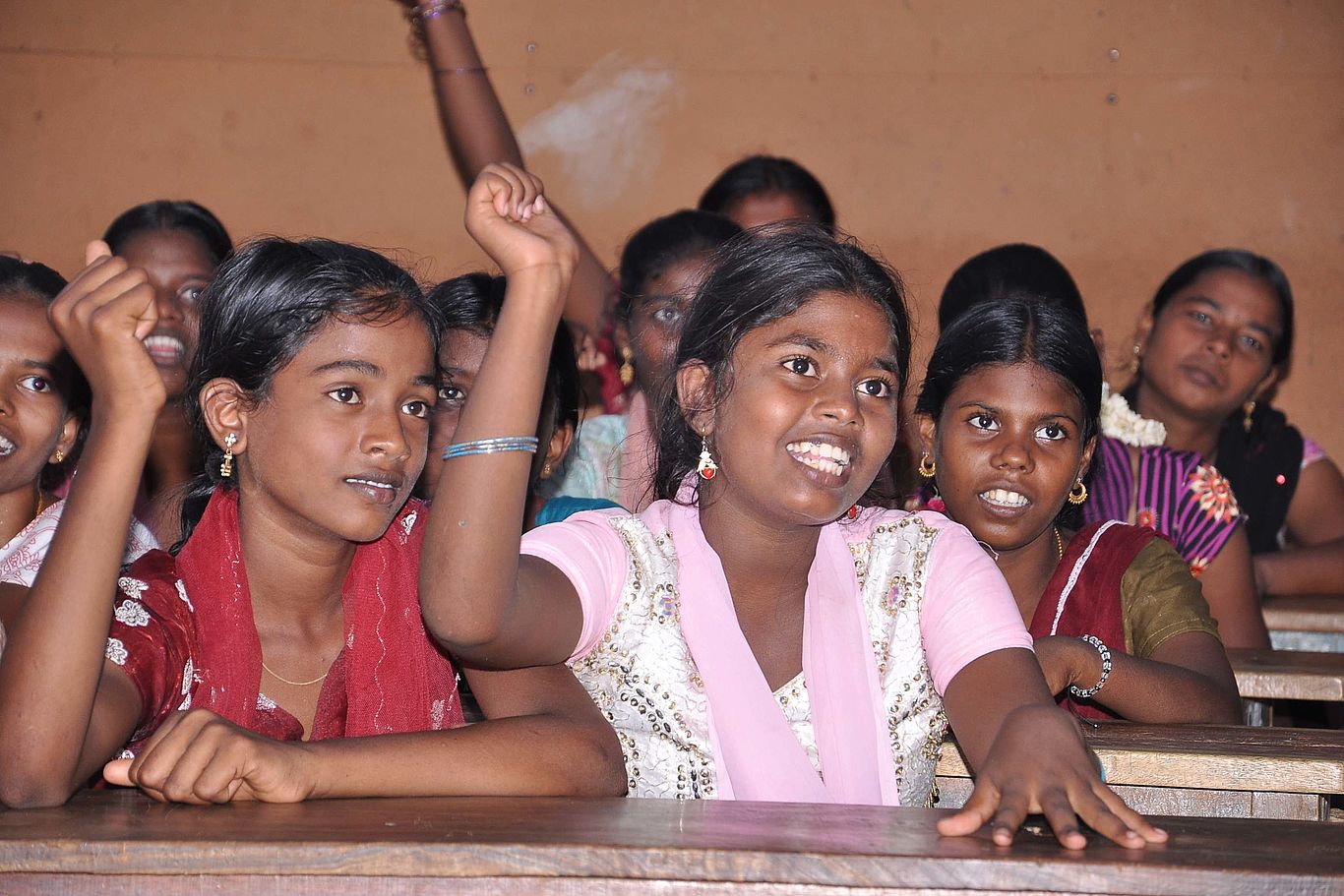 Indien: Schule statt Kinderarbeit/Bild: Van Muhil Viele Mädchen sitzen hintereindander in Schulbänken. Einige Mächen zeigen auf.