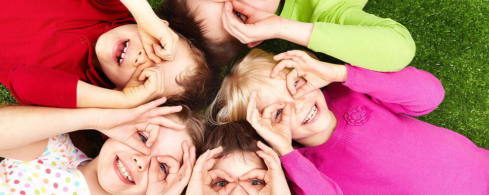 Kinder liegen auf dem Rücken im Kreis. Alle haben Daumen und Ringfinger zusammengetan und halten sie vor ihre Augen, wie eine Brille.