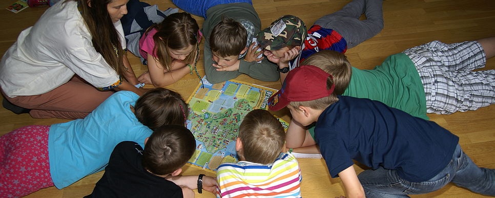 Kinder liegen im Kreis auf dem Boden und schauen auf eine Karte. 