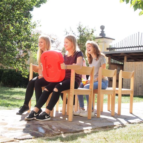 Drei jugendliche Mädchen sitzen auf Stühlen und lachen. Die Stühle sind in Zweier-Reihen hintereinander aufgestellt. 