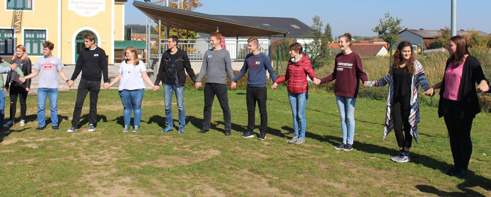 Jugendliche stehen auf einer Wiese im Kreis und halten sich an den Händen.