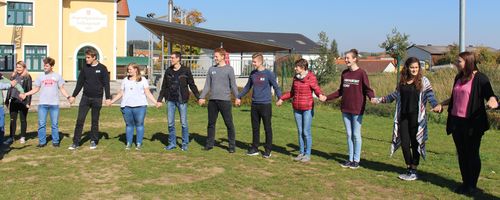 Jugendliche stehen auf einer Wiese im Kreis und halten sich an den Händen.