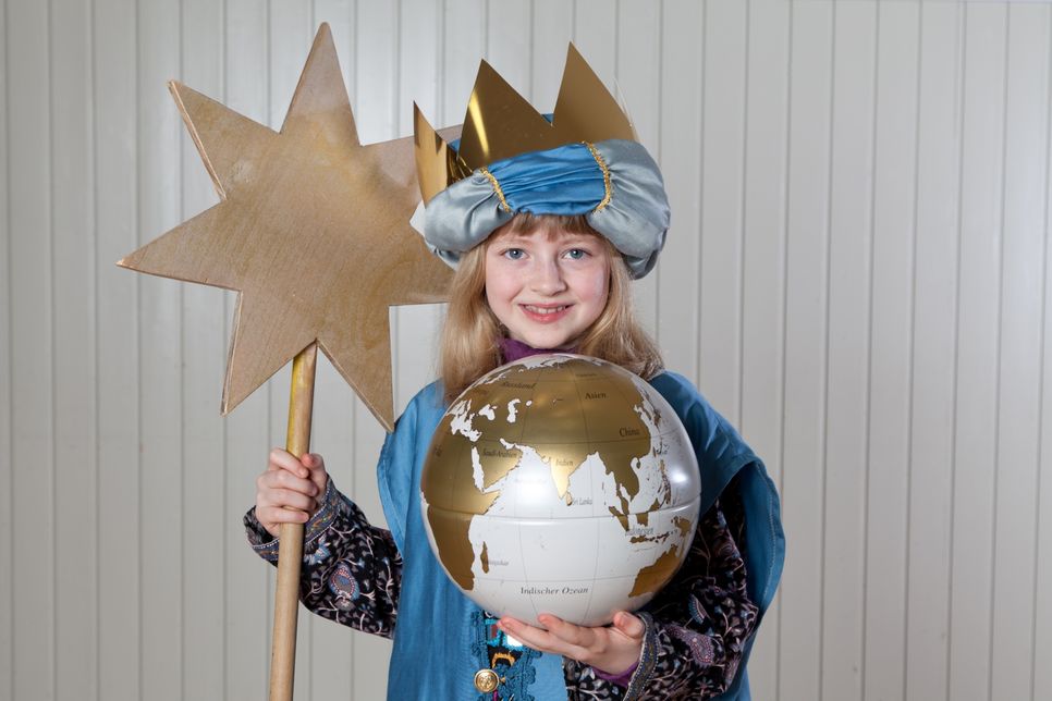 Sternsingerkind hält in einer Hand einen Globus und trägt in der anderen den Stern.