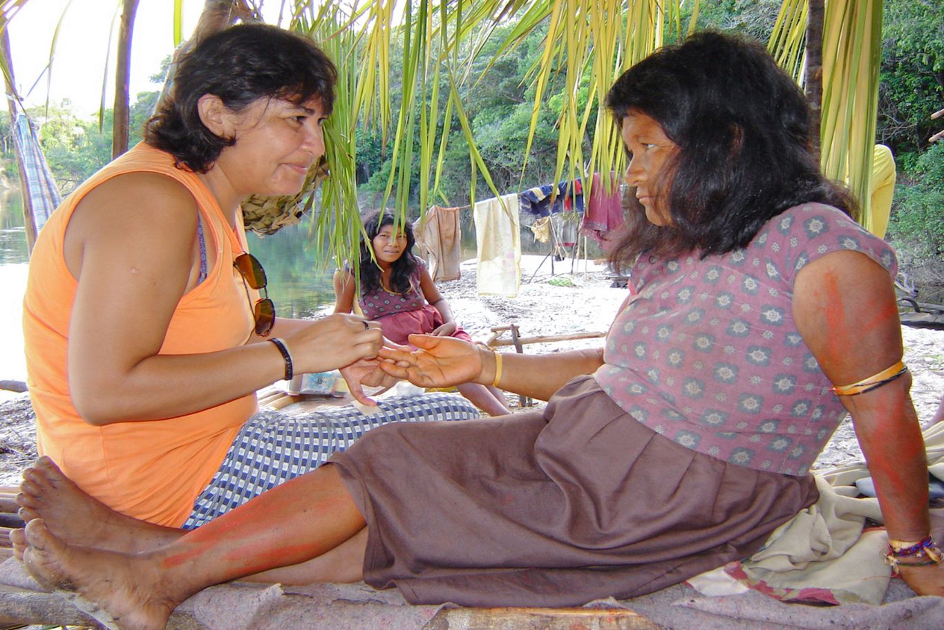 Eine CIMI Mitarbeiterin sitzt neben einer anderen Frau und betreut sie medizinisch. Eine weitere Frau sitzt im Hintergrund.
