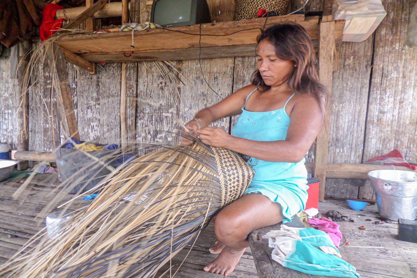 Eine Frau flechtet einen Korb. Die Indigenen können selbstgemachte Produkte (zb. Honig, Copaíba-Öl, geflochtene Körbe) verkaufen und somit fehlende Güter auf lokalen Märkten kaufen.
