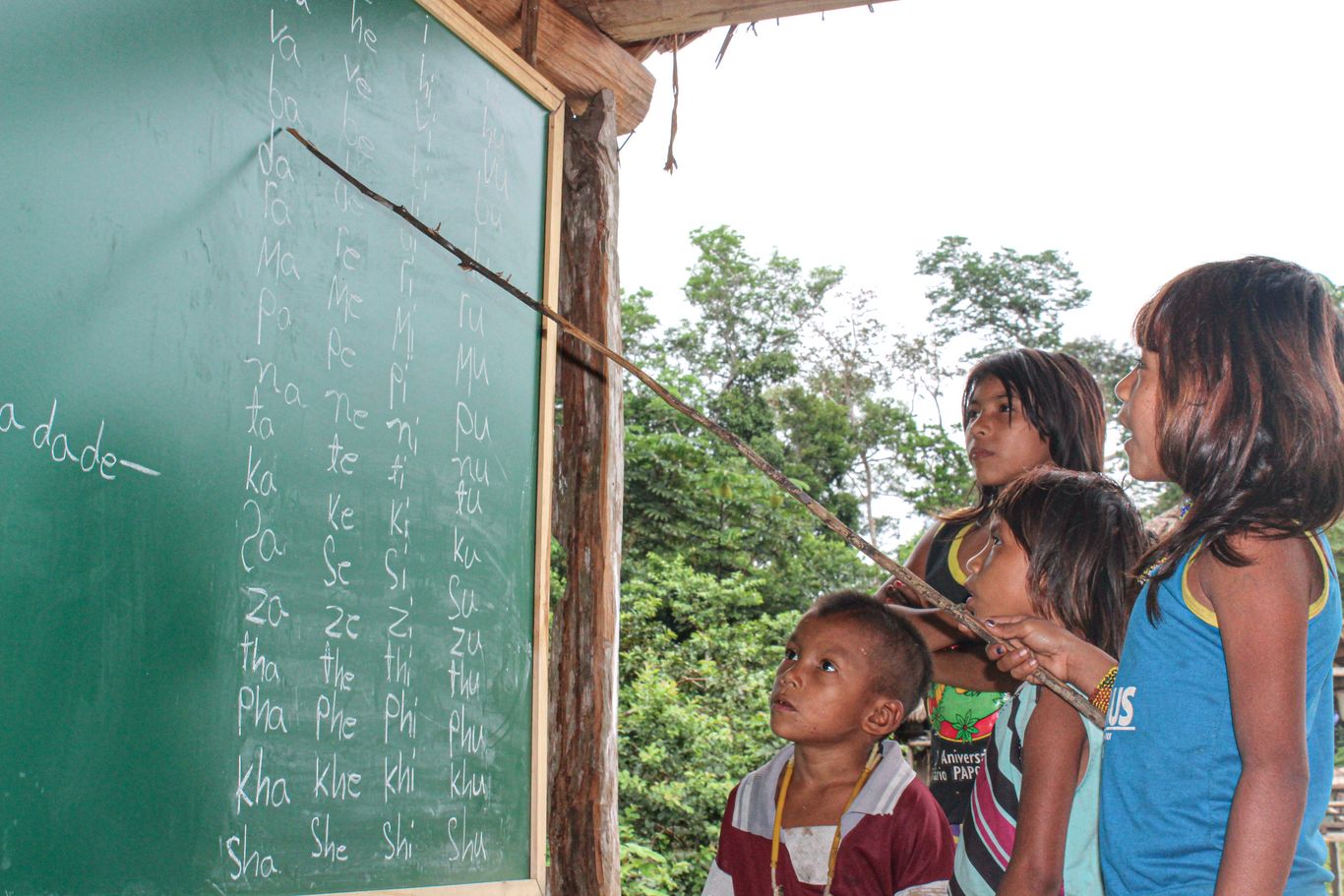 Mehrere Kinder stehen vor einer Schultafel. CIMI fördert die indigene Schulbildung: Mit indigenen Lehrer*innen, Unterricht in der Muttersprache, Portugiesisch als Zweitsprache, traditionellem Wissen zum Leben im Regenwald und den Erhalt der indigenen Kultur.
